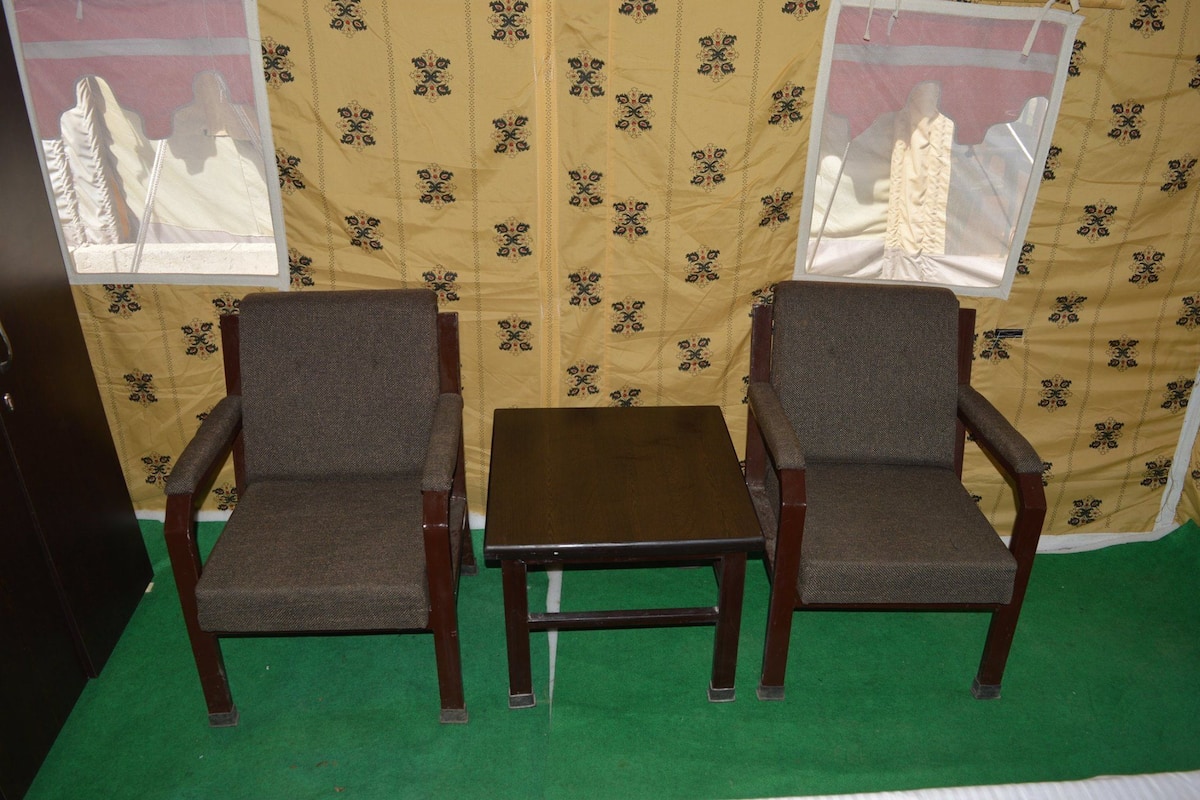 A room with two wooden chairs and a small table, a green carpet, and patterned wallpaper.