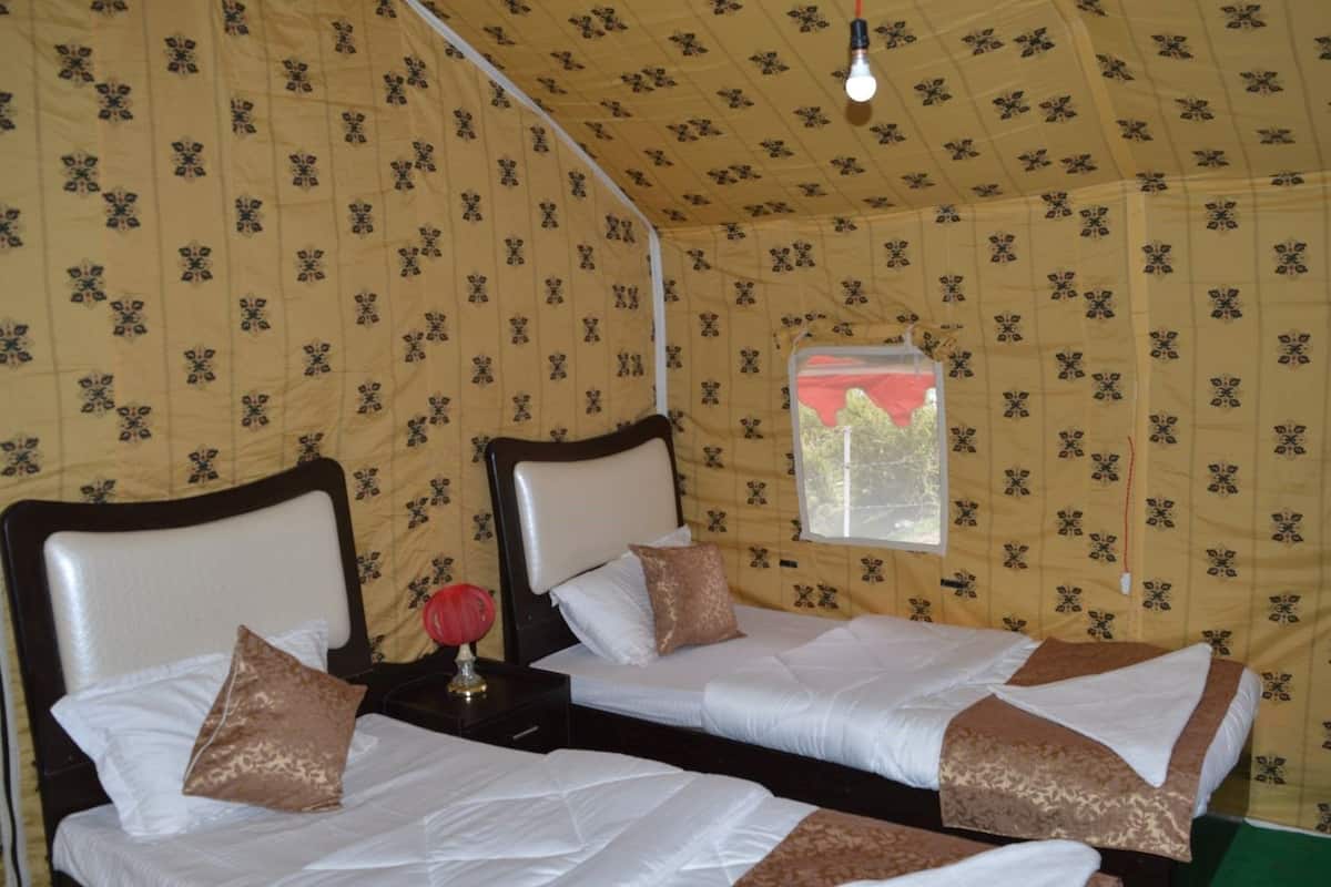 A tented room with two beds, a window, and a nightstand with a lamp.