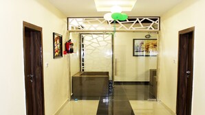 A hallway with a shiny black and white tiled floor, wooden doors on either side, and a ceiling light fixture. - Eco Inn Hotel (Jamnagar)