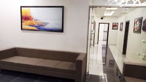 A reception area with a sofa, a framed painting, and a hallway with doors and framed pictures. - Eco Inn Hotel (Jamnagar)