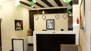A reception area with a reception desk, clocks, and a fire extinguisher. - Eco Inn Hotel (Jamnagar)