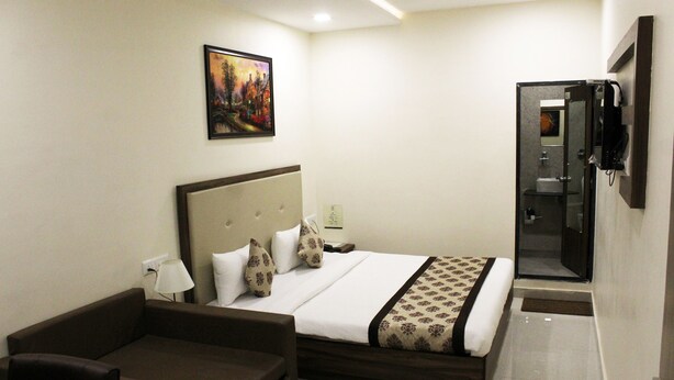 A hotel room with a bed, a sofa, a painting on the wall, and a bathroom door. - Eco Inn Hotel (Jamnagar)