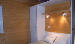 Une petite pièce chaleureuse aux murs en bois, avec un lit recouvert de linge de maison blanc et une tête de lit en bois dotée d’un éclairage intégré.