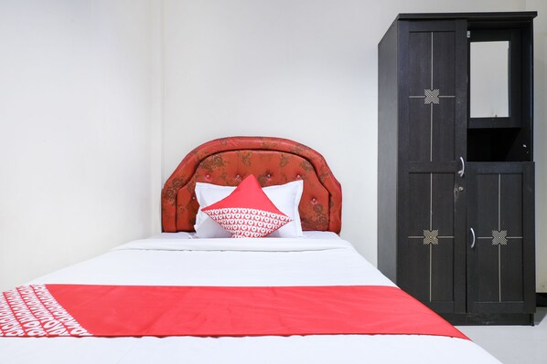 Una cama con una colcha rojo y blanco, una almohada roja y un armario de madera oscura con un espejo.