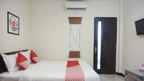 Een hotelkamer met een bed, een raam met gordijnen, een airconditioner, een deur en een televisie aan de muur.