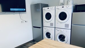 Ein Waschraum mit gestapelten, frontgeladenen Waschmaschinen und Trocknern, einem Holztisch und einem an der Wand montierten Fernseher.