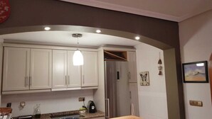 Una cocina compacta con armarios blancos, un refrigerador de acero inoxidable y una lámpara colgante.