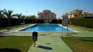 Una piscina rectangular con solárium de azulejos, rodeada por césped y un seto.