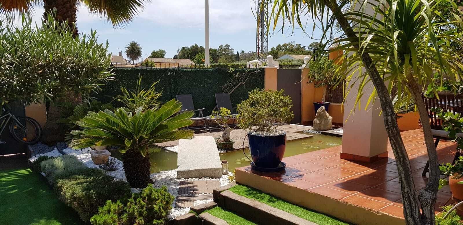 Un espace extérieur aménagé avec soin, comprenant une petite fontaine, des sièges et divers pots de plantes.