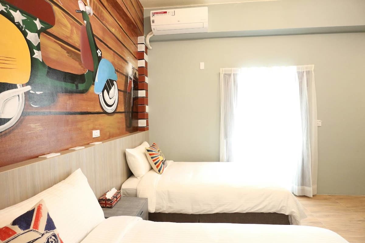 A hotel room with two beds, a mural on the wall, and a window with curtains.