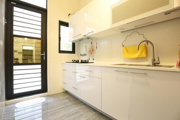 A modern kitchen with white cabinets, a stainless steel sink, and a yellow towel hanging on the wall.