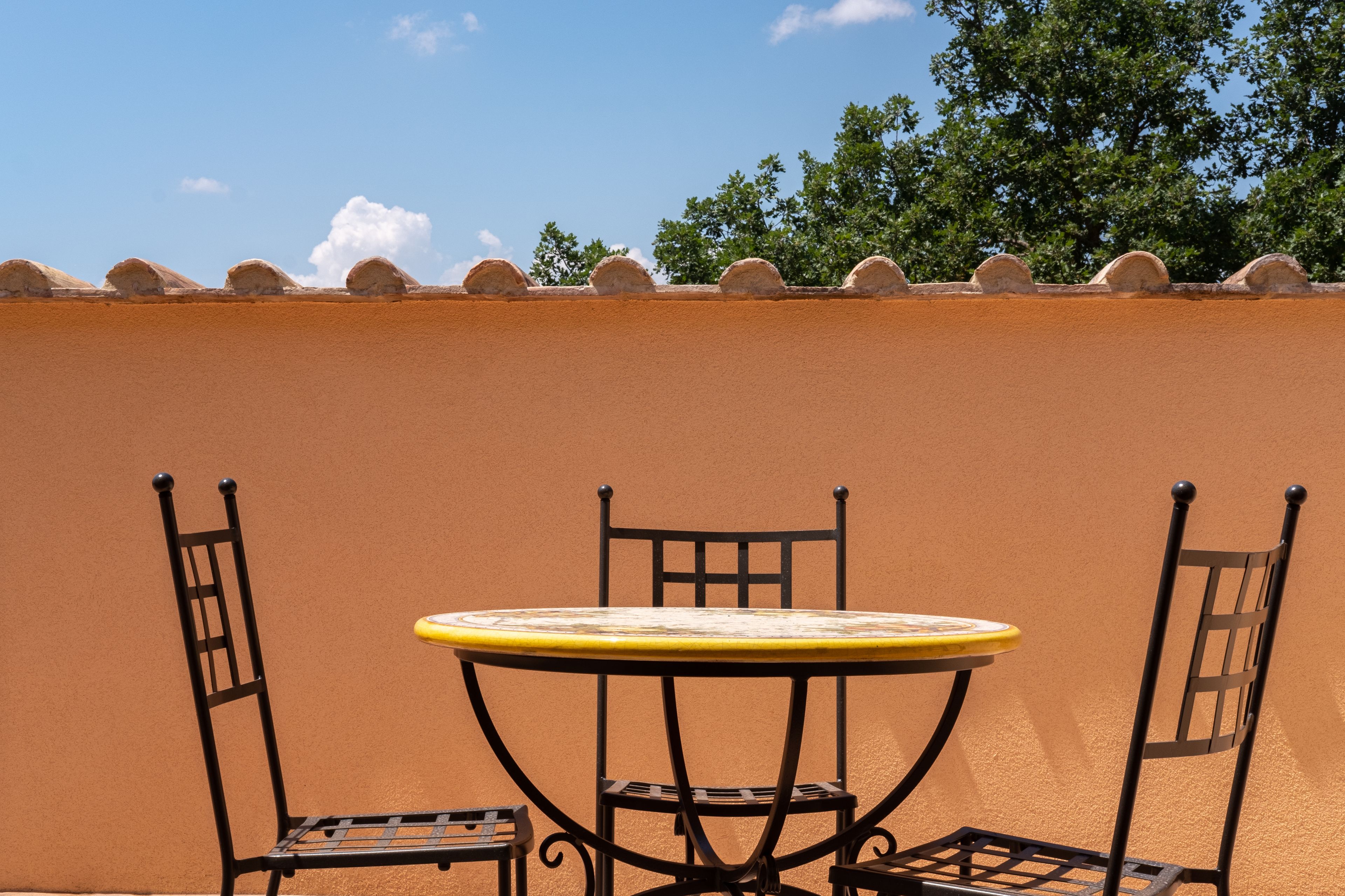 A round table with two chairs, set against a plain wall with a series of rounded stone structures at the top.