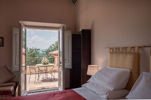 Ein Hotelzimmer mit Bett, Nachttisch, Lampe und Blick auf eine Terrasse mit Tisch und Stühlen.