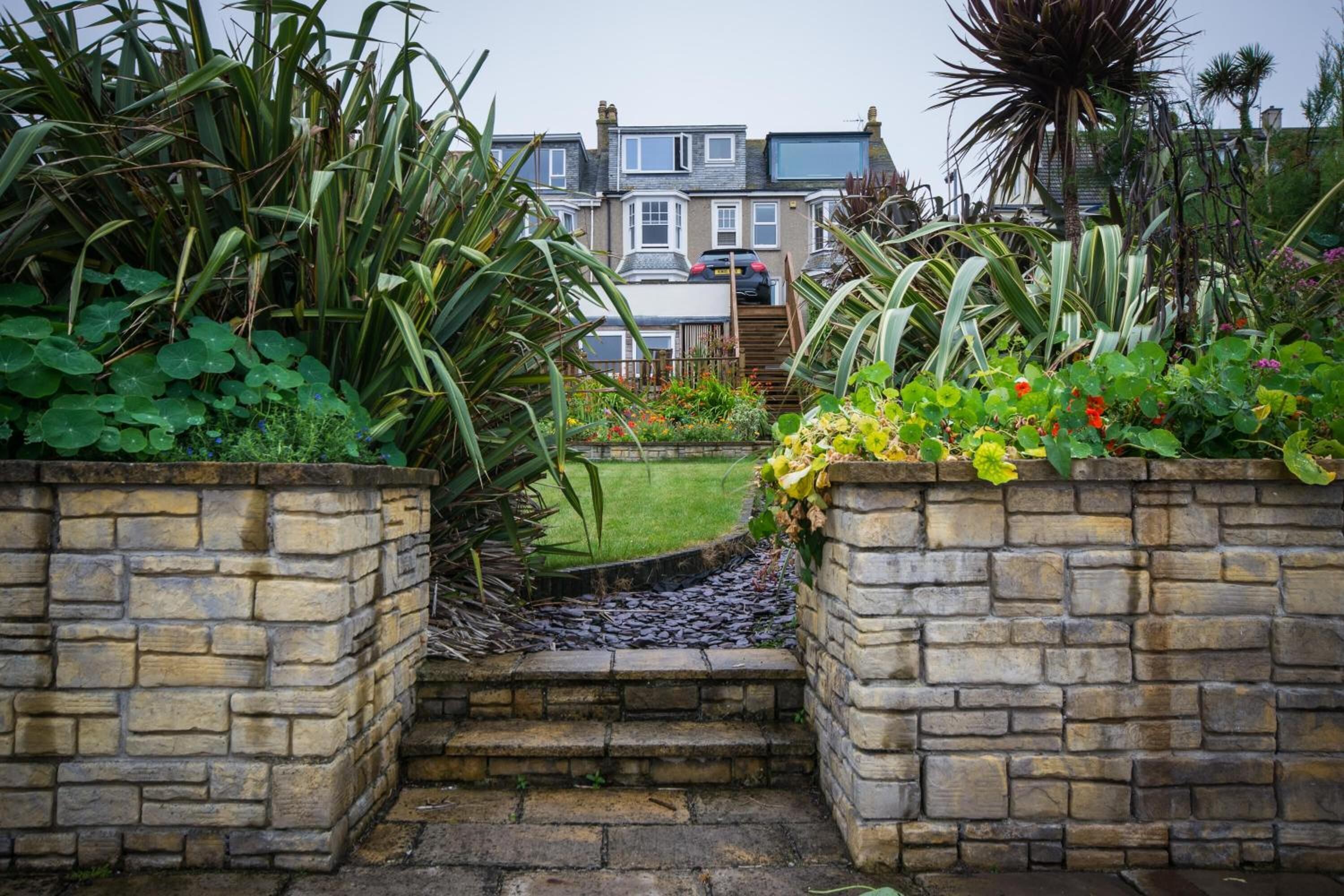 A stone pathway leading to a residential area with a lawn and a variety of plants.