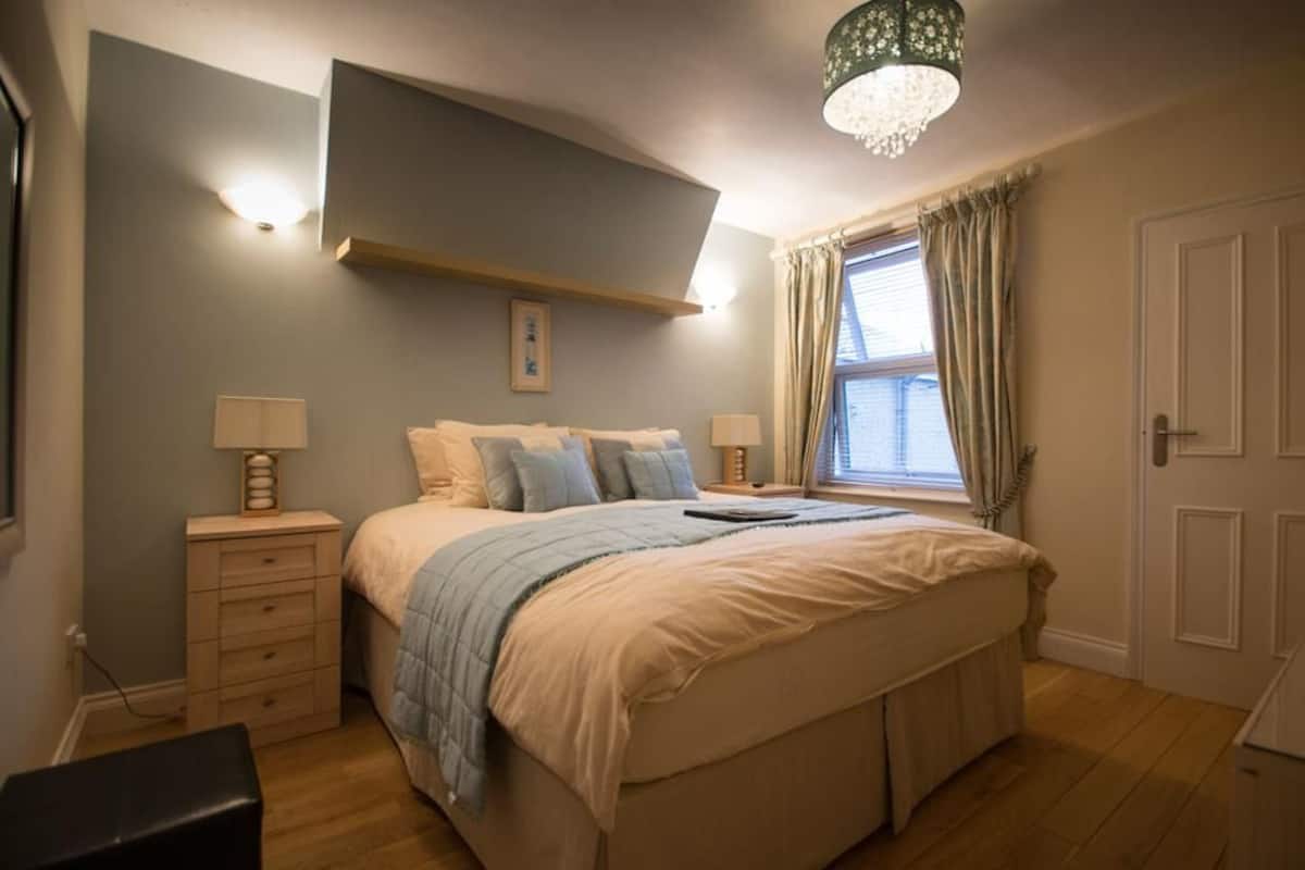A bedroom with a large bed, bedside tables, a hanging light fixture, and a window with curtains.