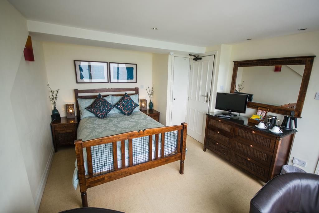 A bedroom with a wooden bed, a dresser, a television, and a mirror.