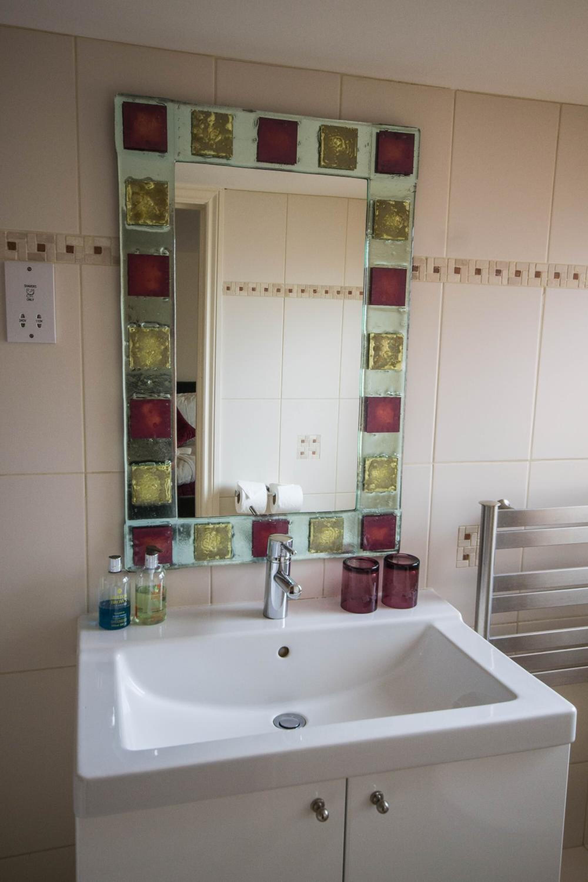 A bathroom with a white sink, a mirror with a decorative frame, and a towel rack.