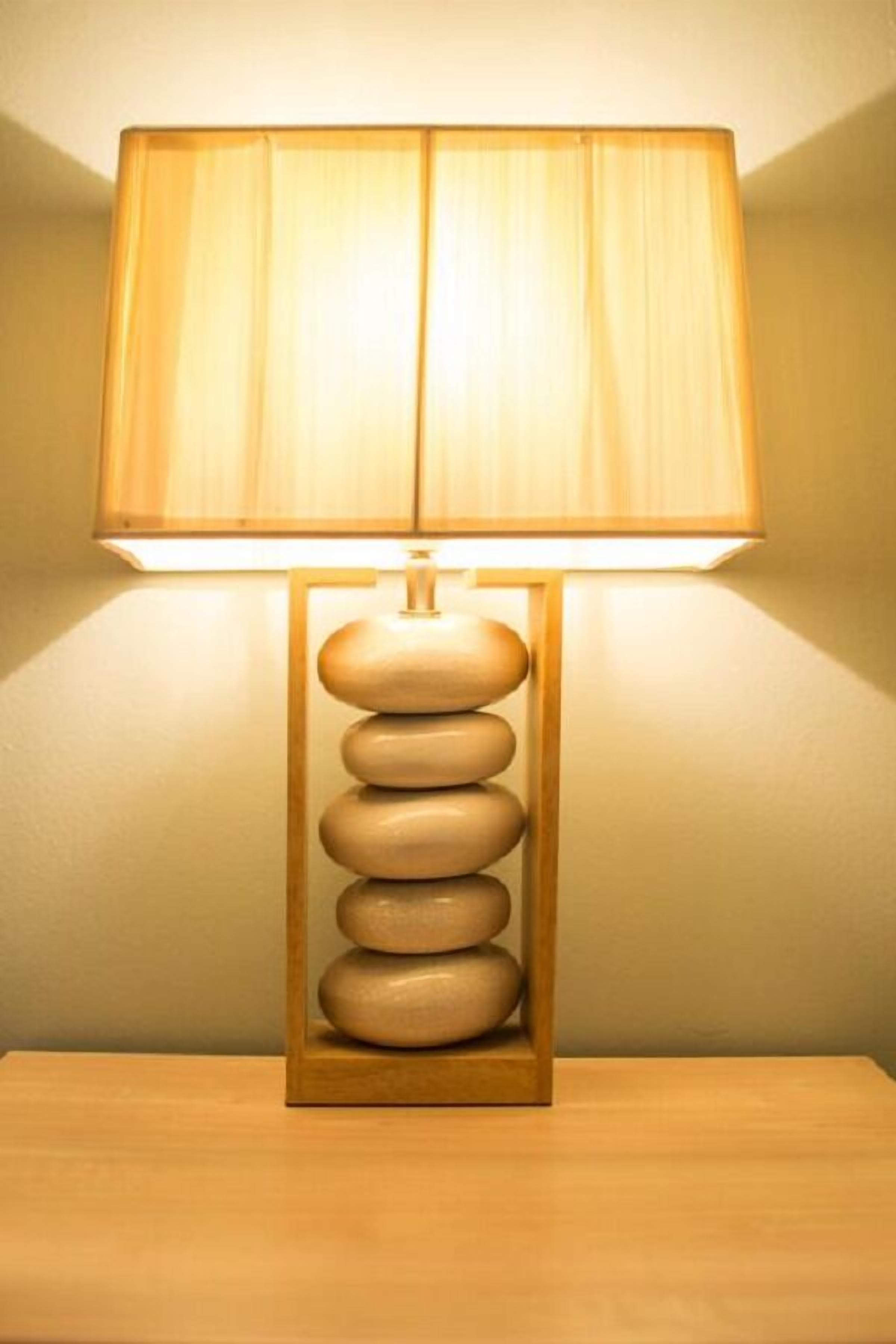 A lamp with a wooden base and a beige lampshade on a wooden table.