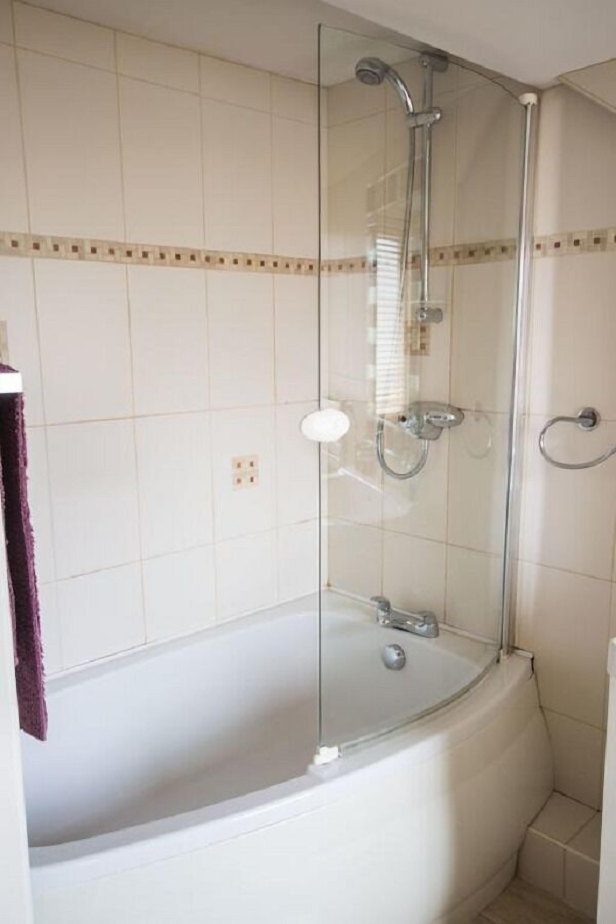 Een douchecabine met glazen wanden, een bad, betegelde wanden en een zichtbare douchekop.