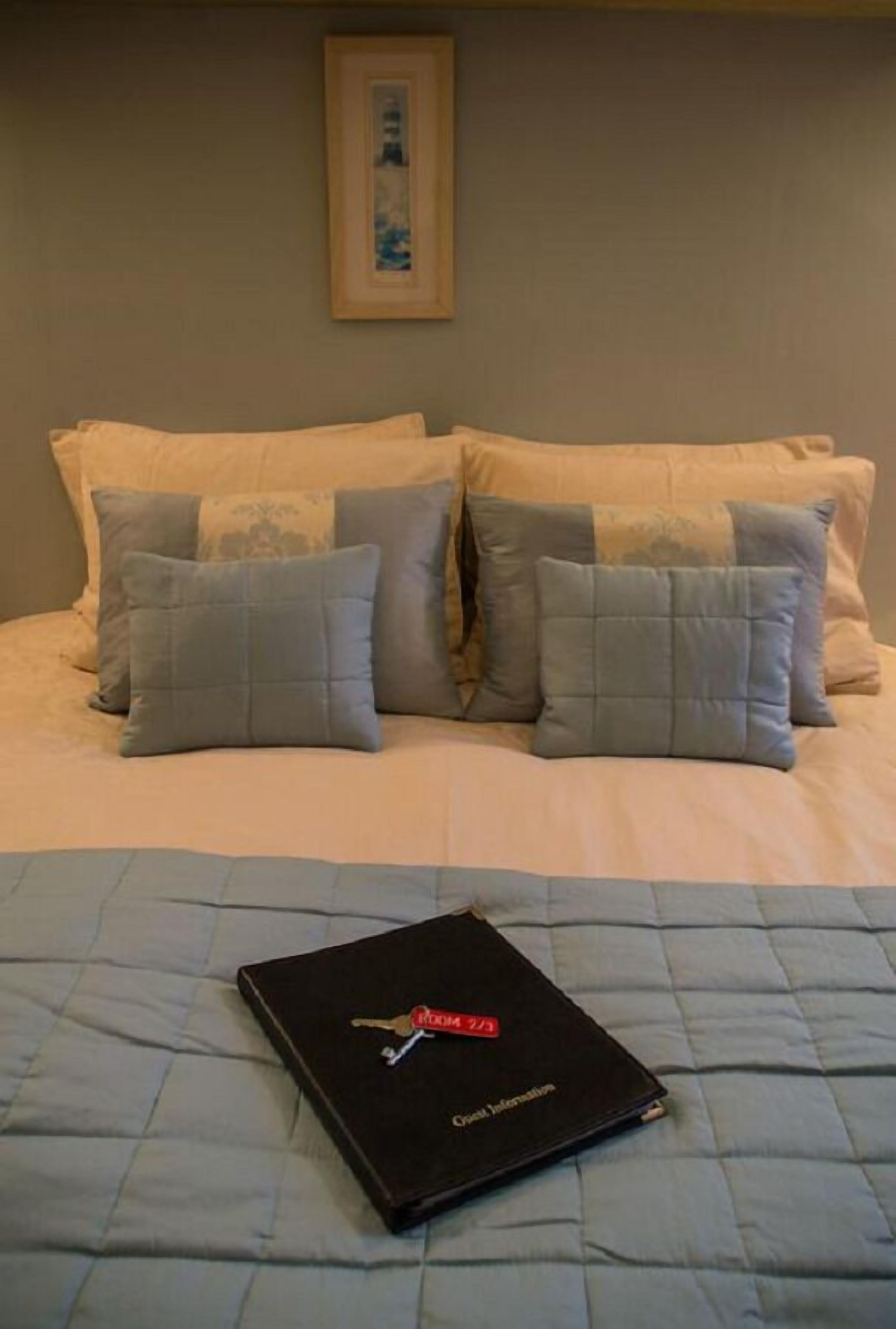 Een bed met een gewatteerde spreidek en meerdere kussens, een ingelijste foto aan de muur en een boek met de titel “Guest Information” op het bed.