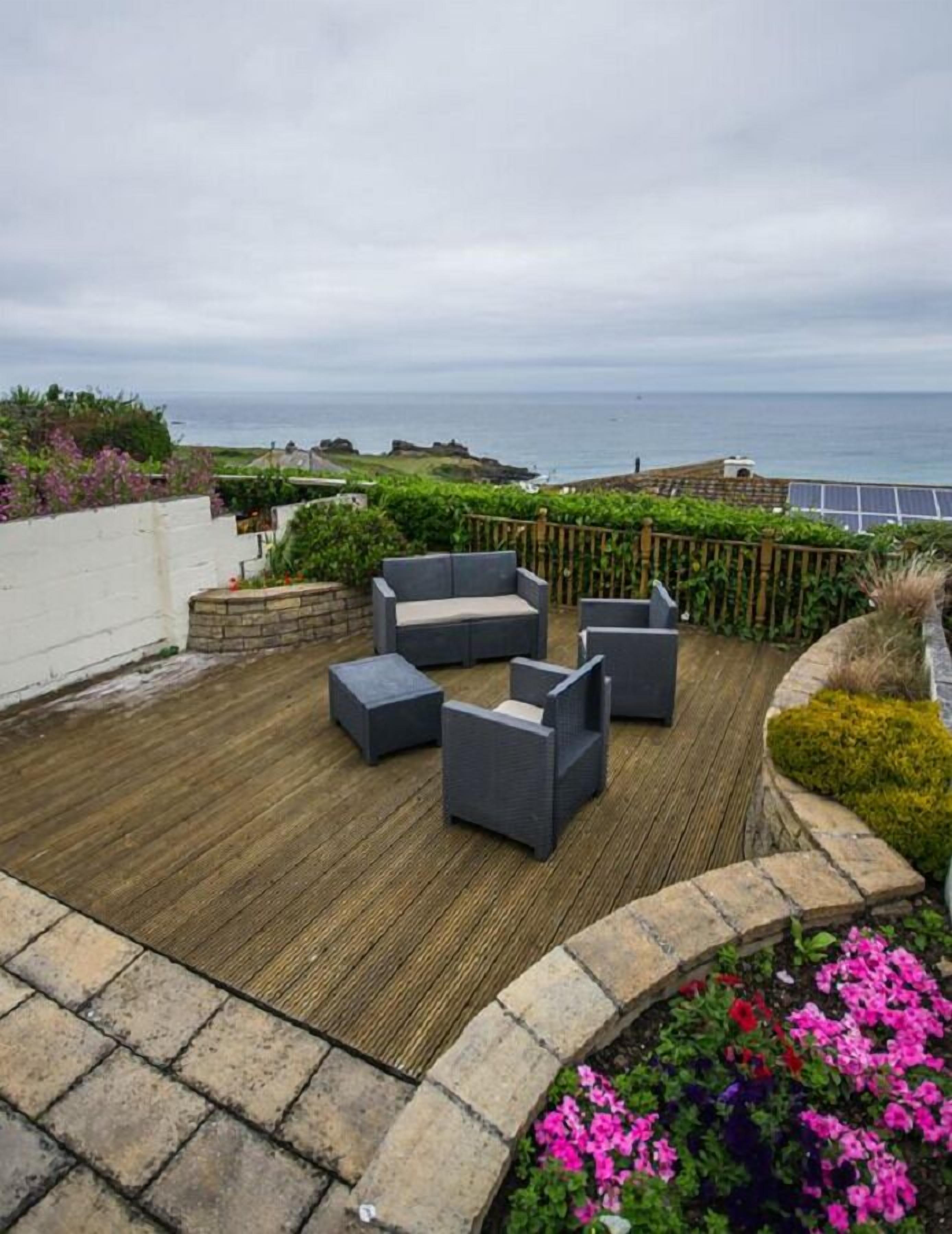 Una terraza en la azotea con mobiliario exterior, vistas al océano y un jardín con flores.