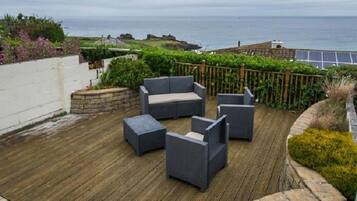 Una terraza en la azotea con mobiliario exterior, vistas al océano y un jardín con flores.