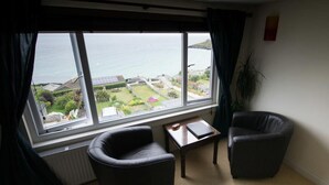 Een kamer met twee stoelen, een tafeltje en uitzicht op zee en groen.