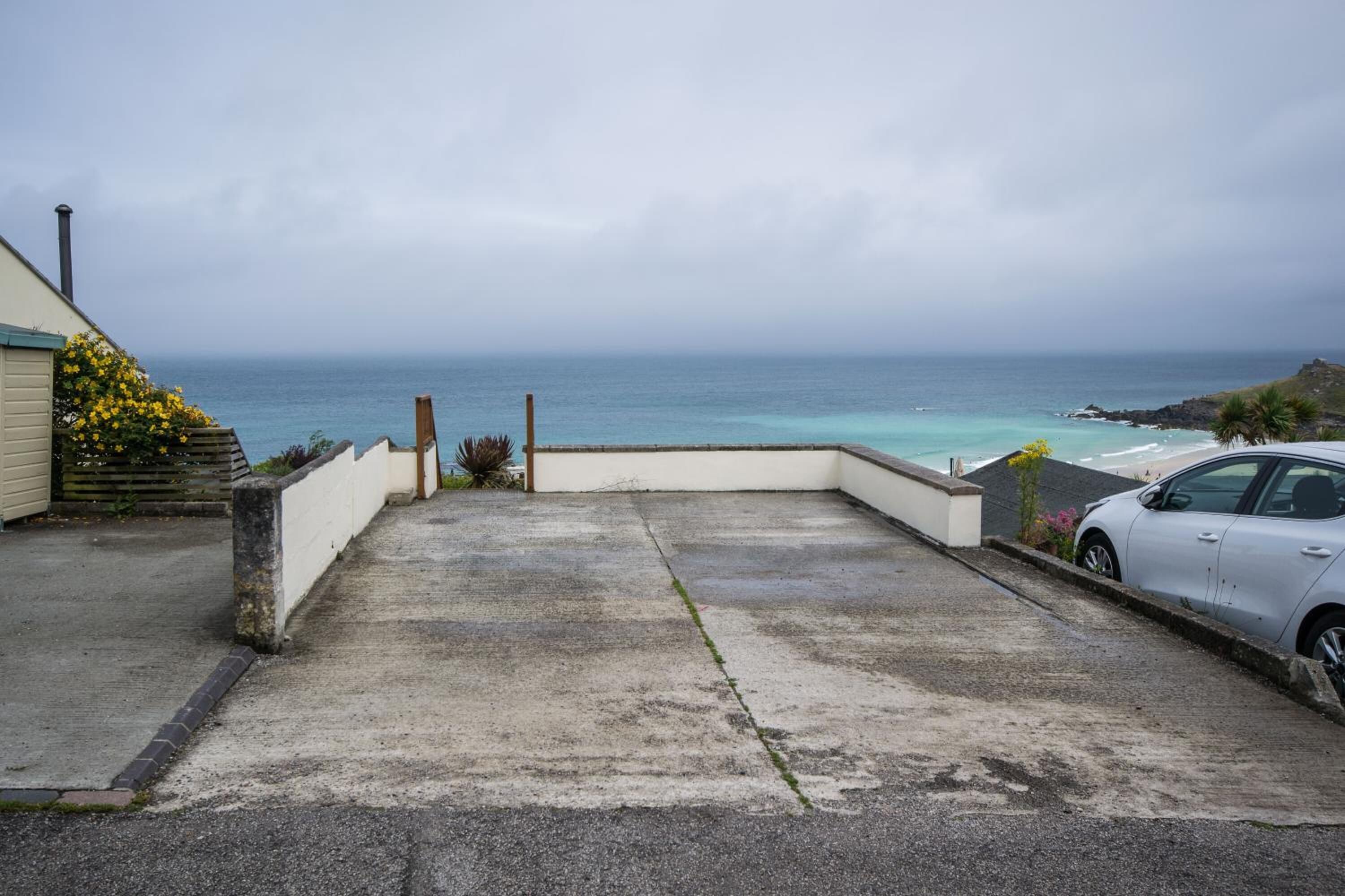 Une allée en béton mène à une zone côtière, et une voiture est garée sur le côté droit.