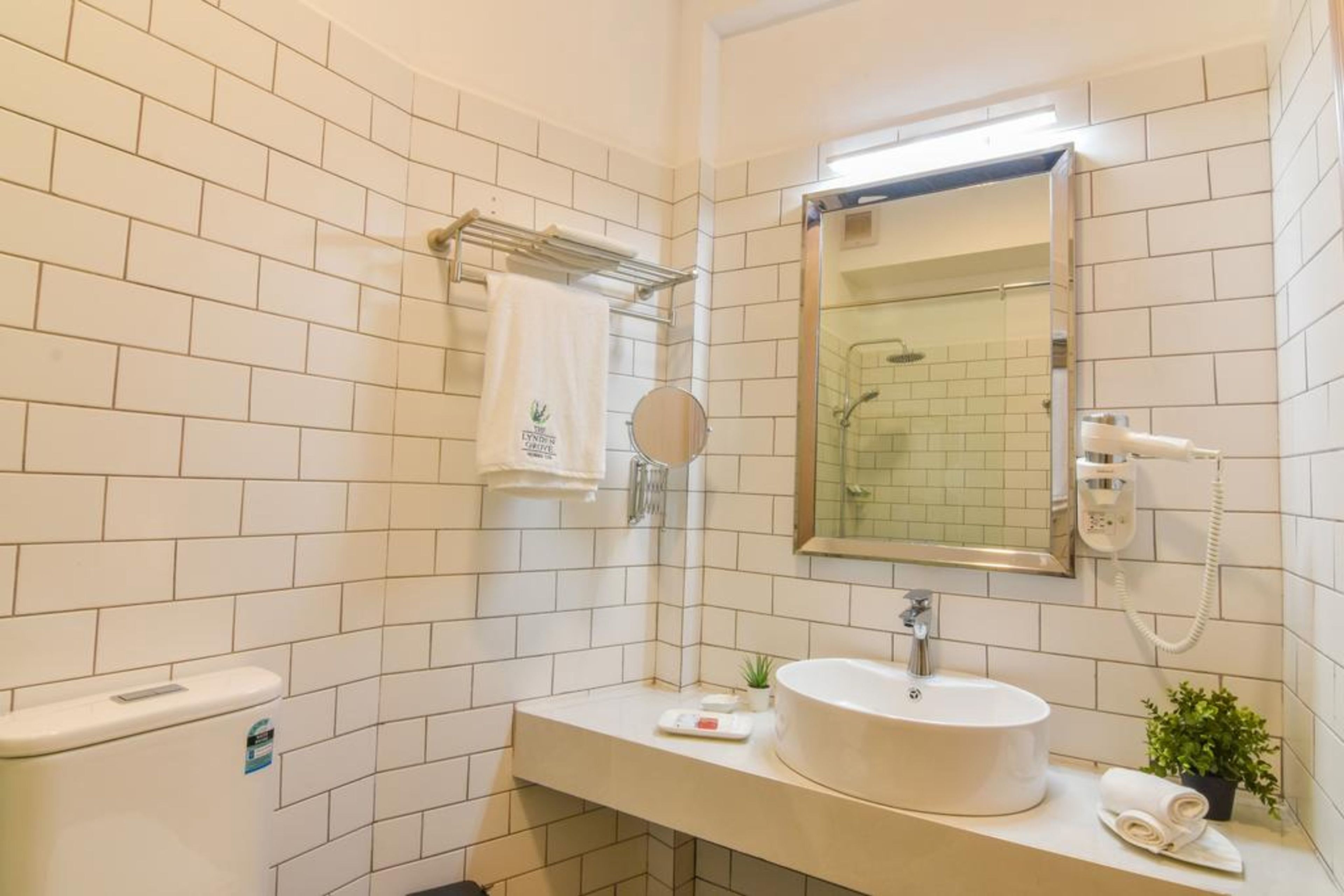 A modern bathroom with white tiled walls, a round sink, a handheld showerhead, a towel rack, and a mirror.