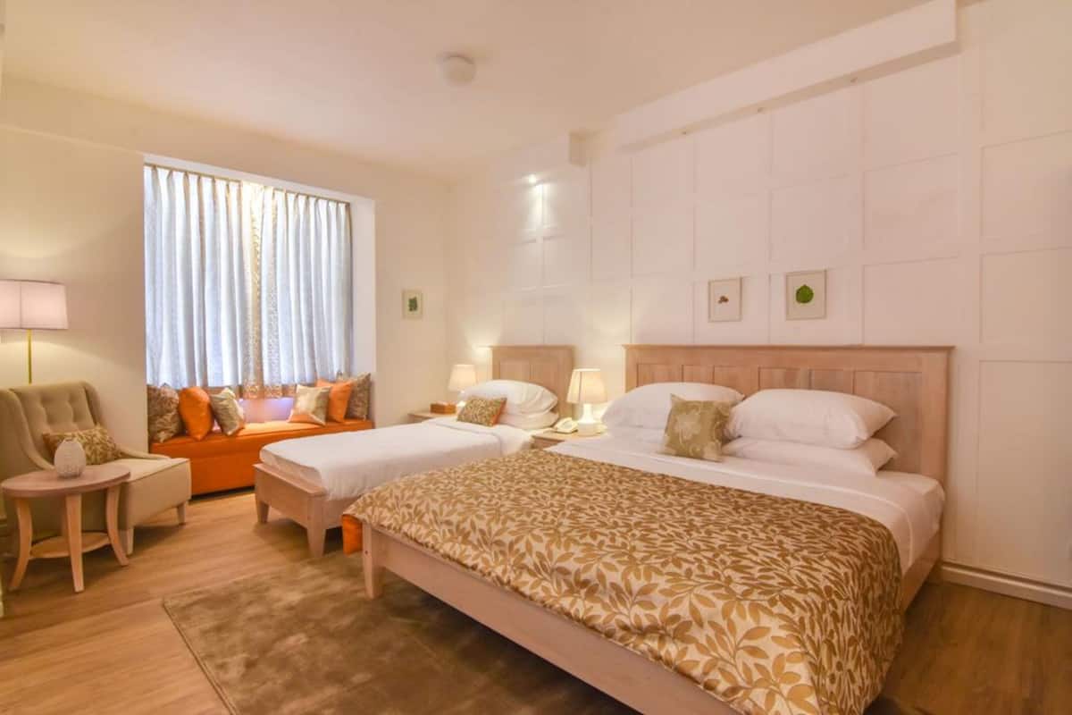 Une chambre d’hôtel avec deux lits, un canapé, une petite table et une fenêtre avec des rideaux.