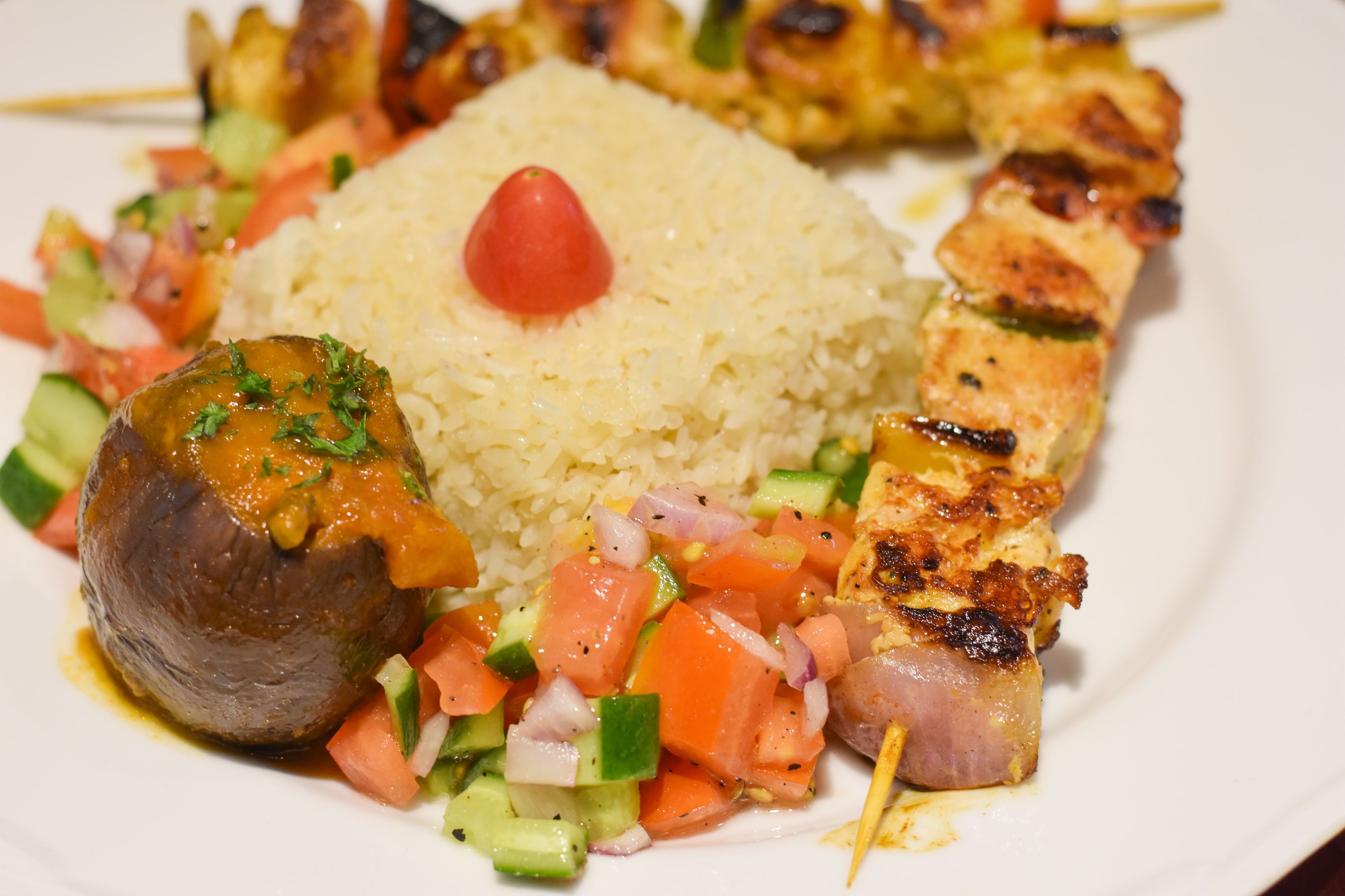 Un plato de comida con arroz, carne a la parrilla, un vegetal a la plancha y una guarnición de tomate.