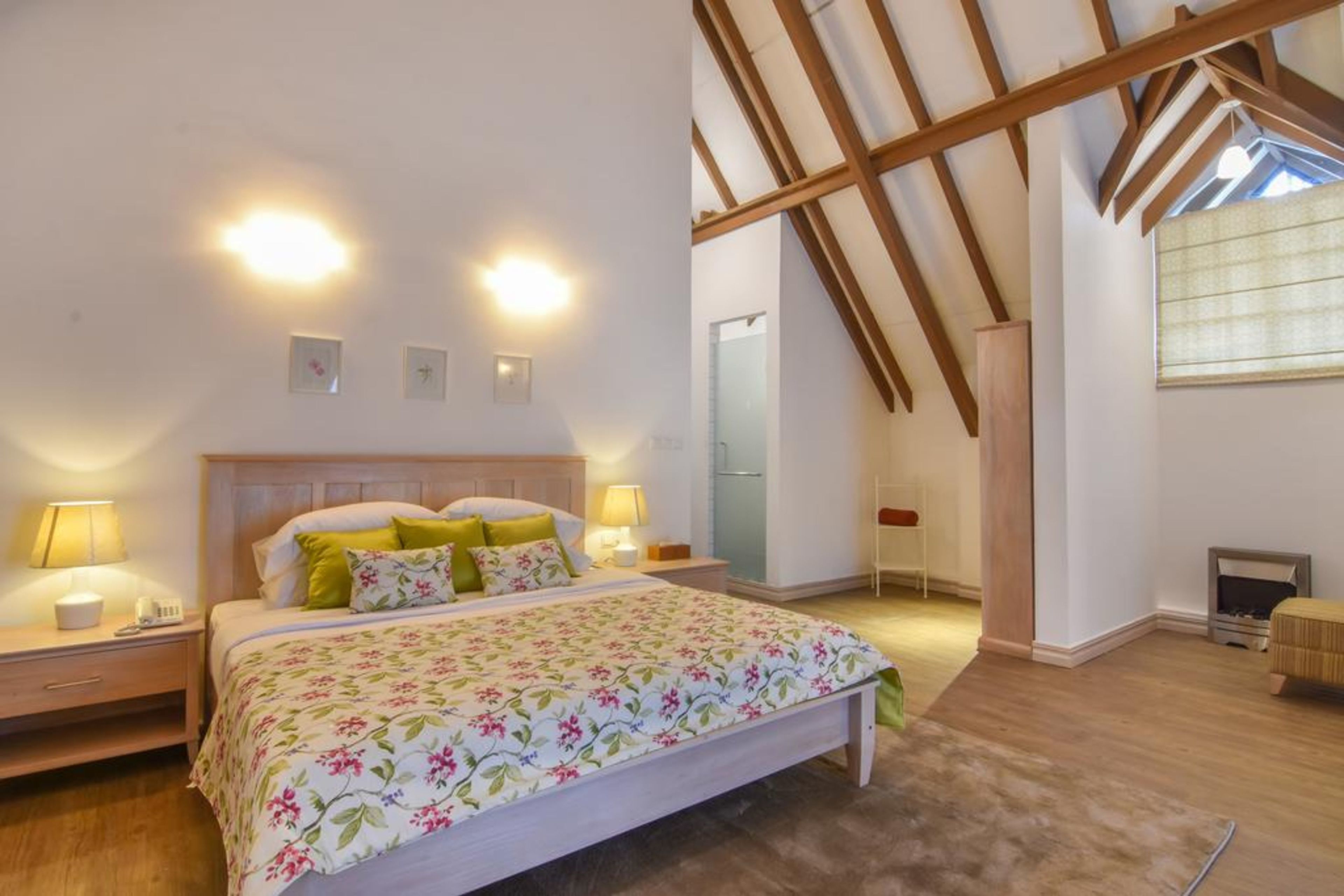 A bedroom with a wooden ceiling, a bed with floral bedding, bedside lamps, and a small wooden bench.