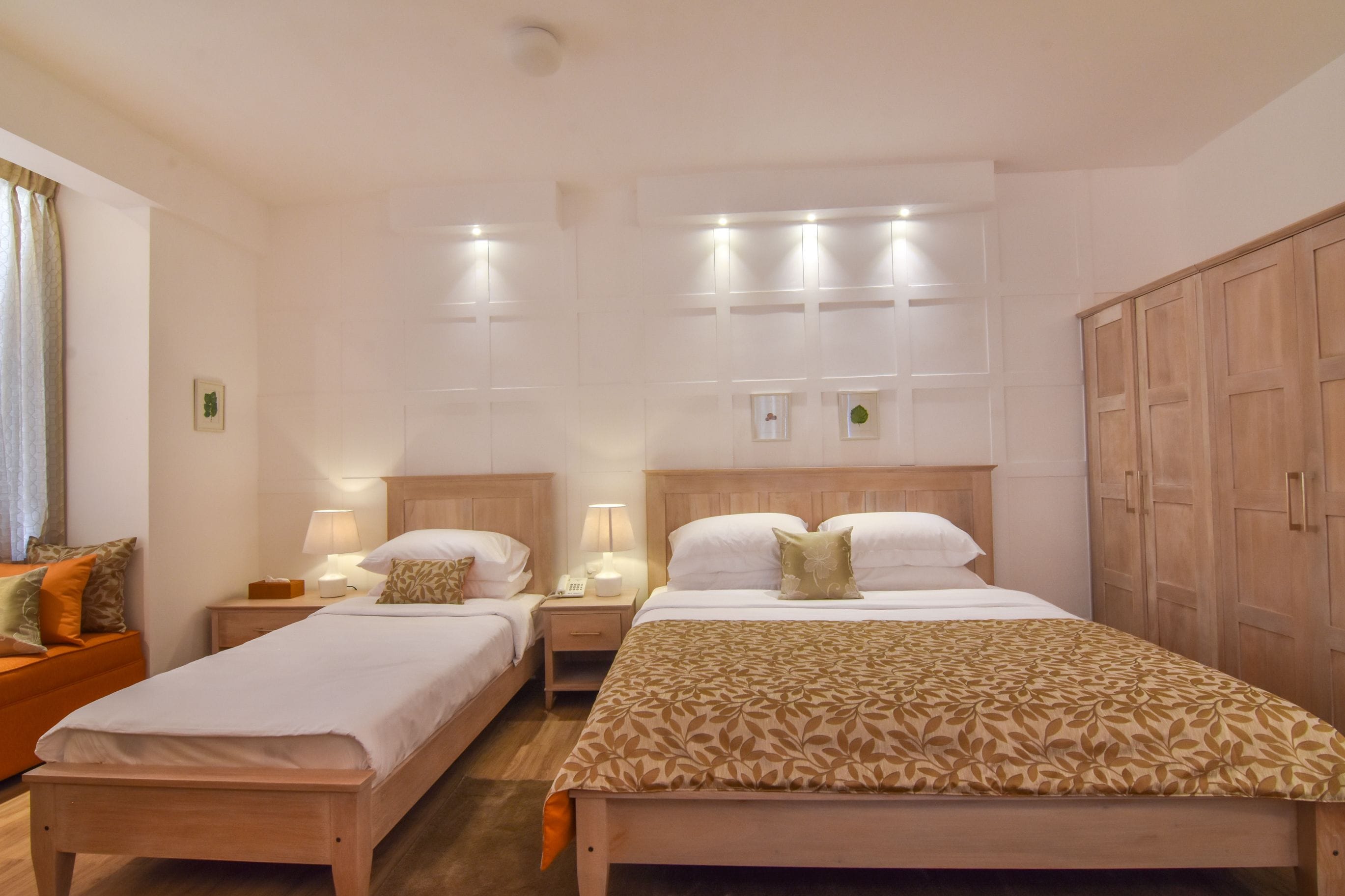 A hotel room with two single beds, a wooden wardrobe, and a nightstand with a lamp.