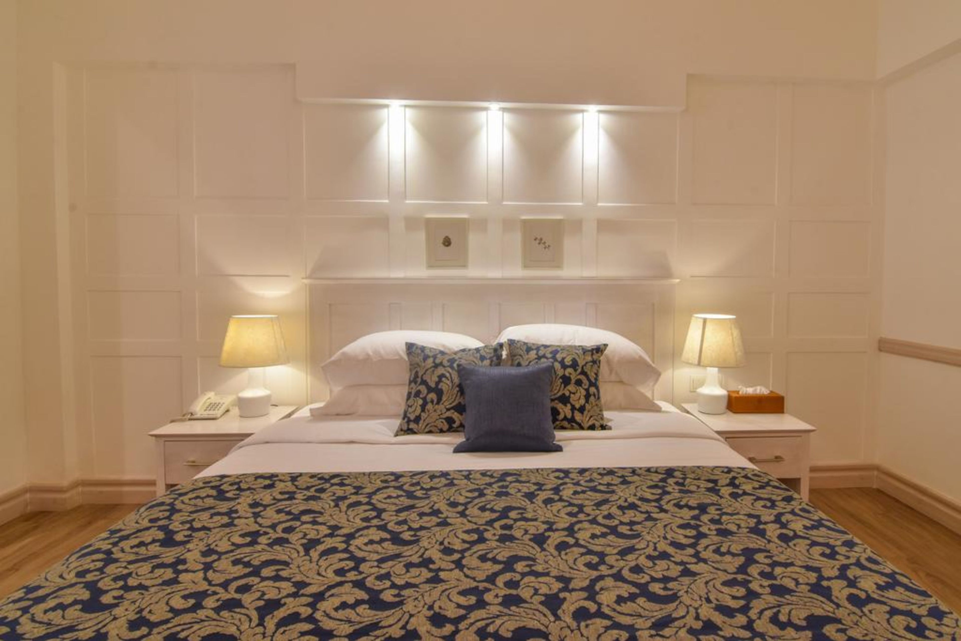 A neatly made bed with a patterned bedspread, two bedside lamps, and a nightstand with a telephone.