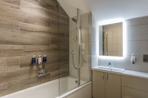A modern bathroom with a glass-enclosed shower, wooden wall tiles, and a built-in sink with a mirror above it.