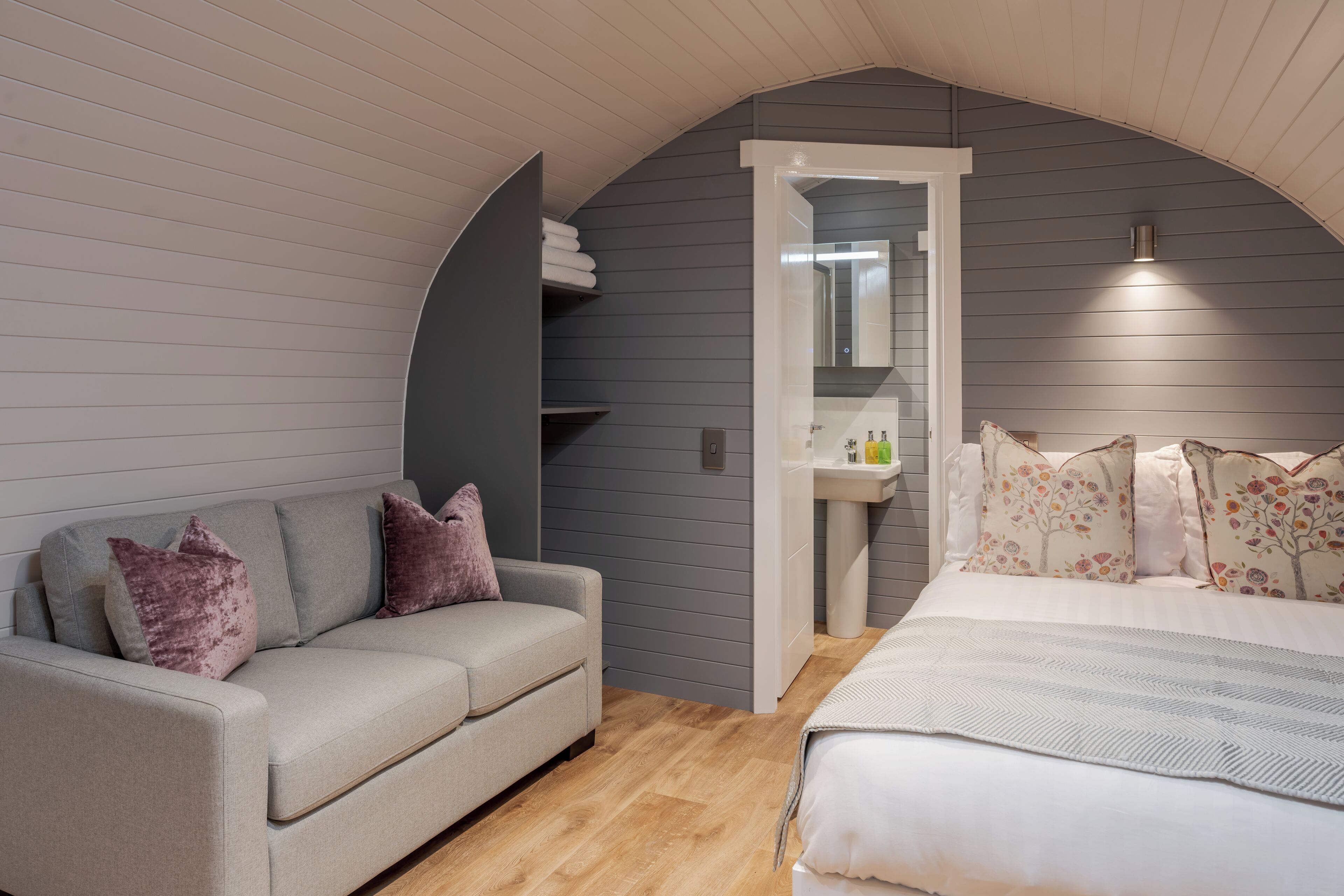 Un dormitorio con cama, sofá, un baño pequeño y un techo curvo.