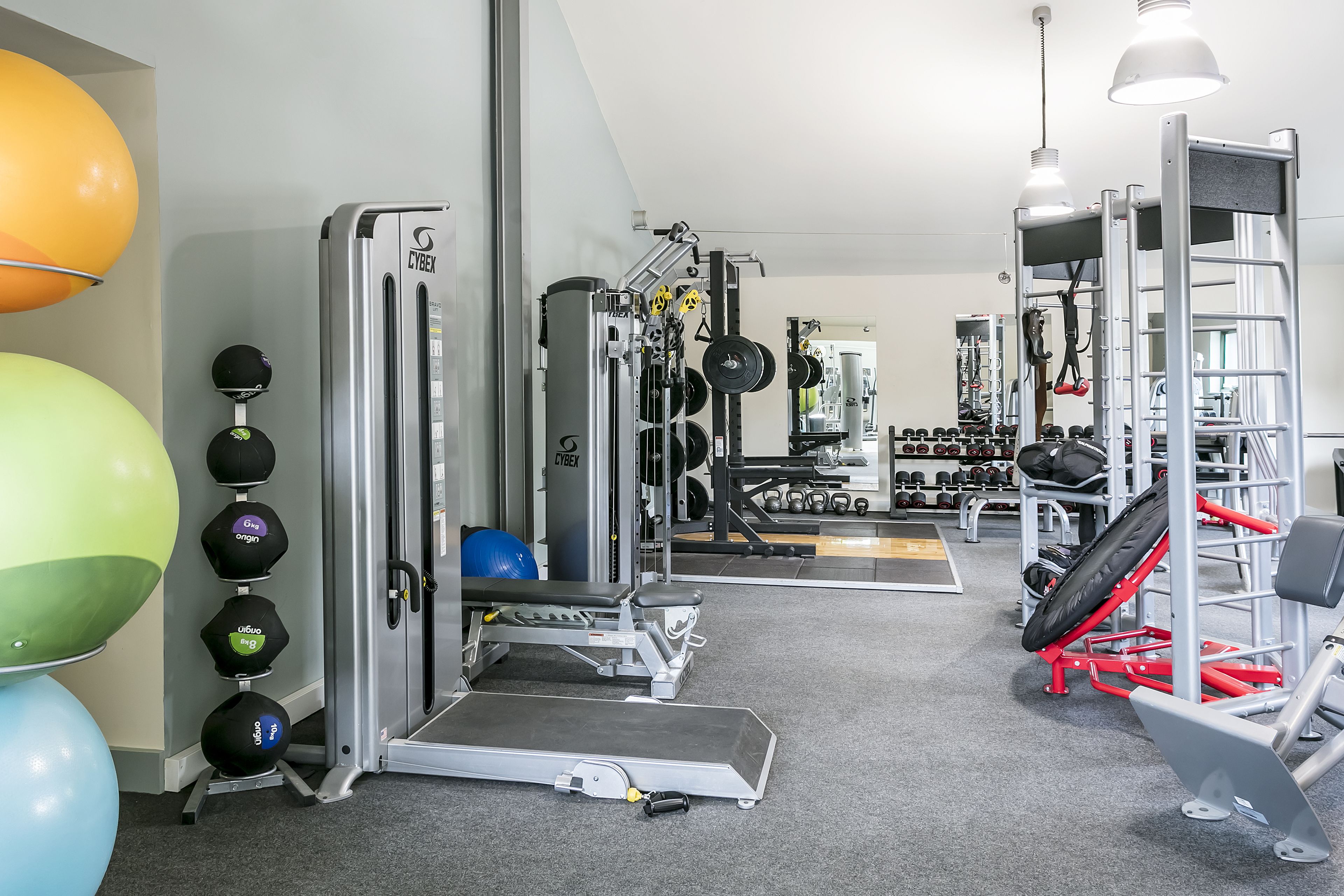 A gym with weightlifting equipment, exercise balls, and dumbbells.