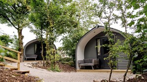 Dos cabañas de forma abovedada con mobiliario exterior, rodeadas de árboles y caminos de grava.