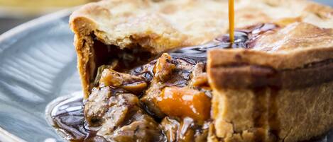 A close-up of a meat pie with gravy being poured over it, placed on a plate.