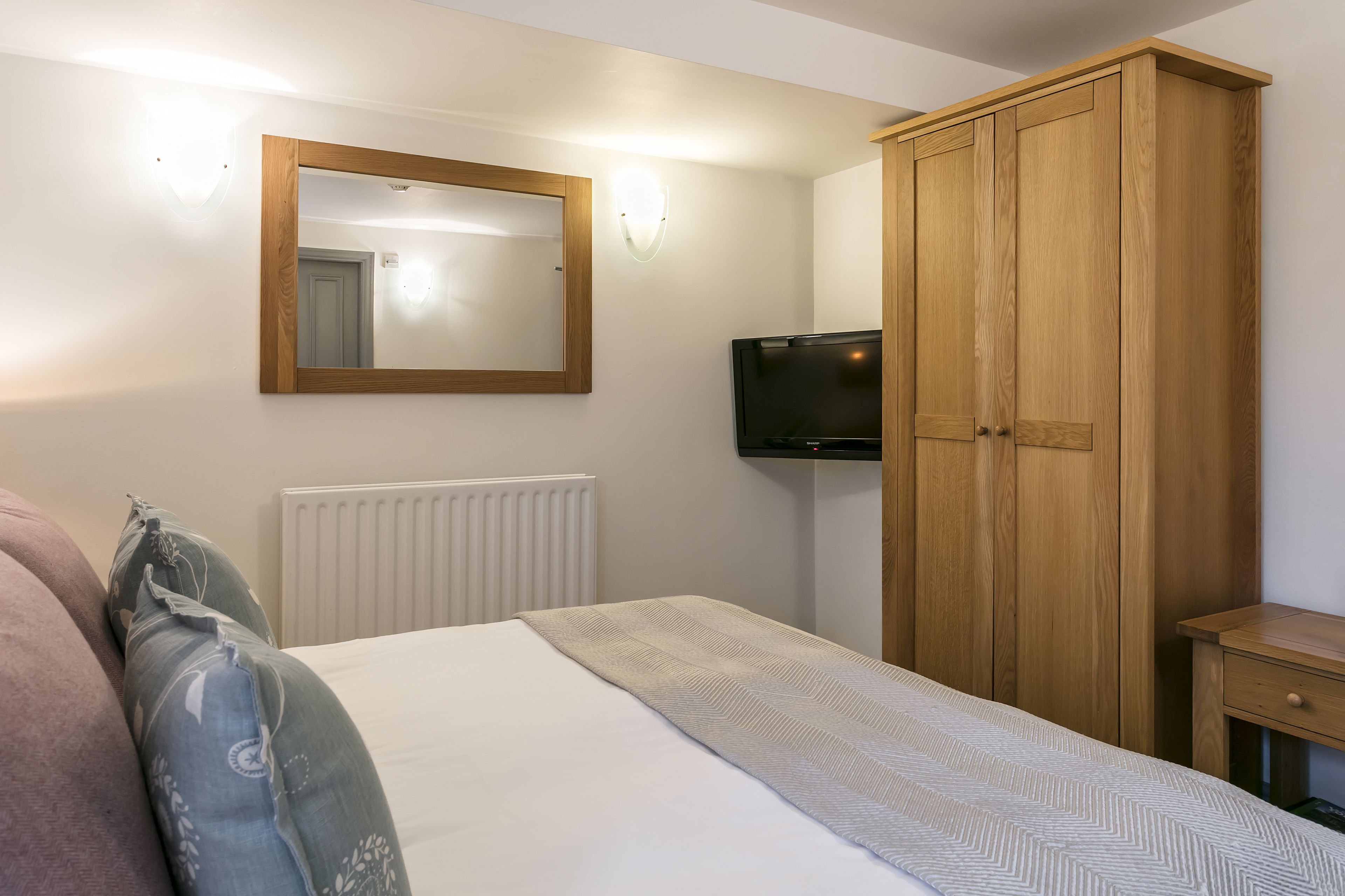 A bedroom with a bed, a wooden wardrobe, a television, and a mirror.