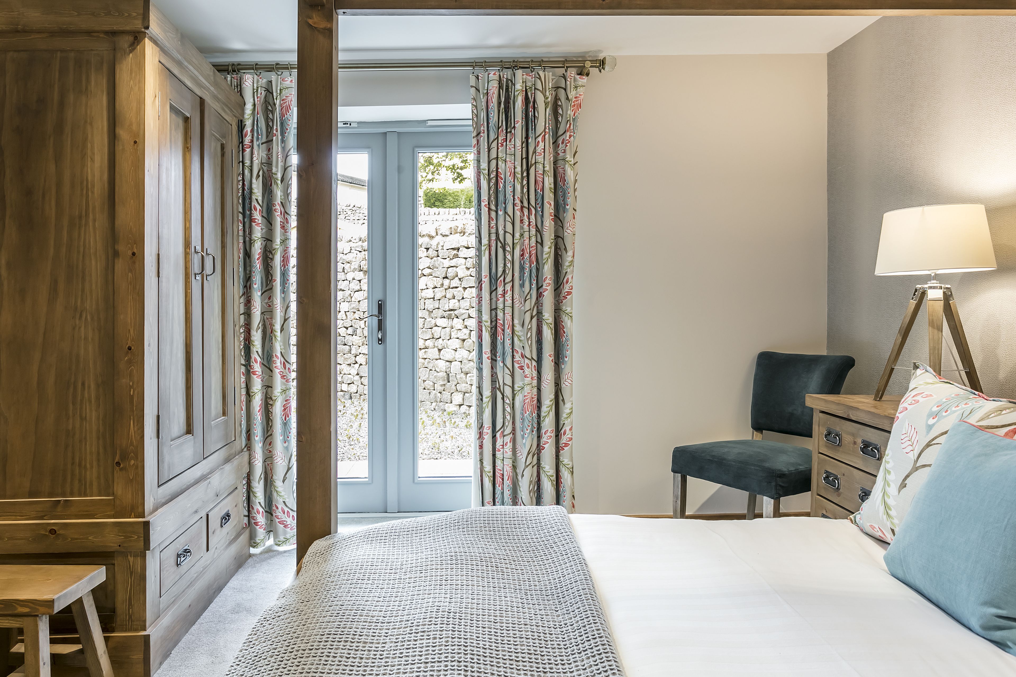 A bedroom with a bed, a wooden wardrobe, a desk with a chair, and a lamp.