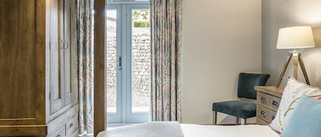 A bedroom with a bed, a wooden wardrobe, a desk with a chair, and a lamp.