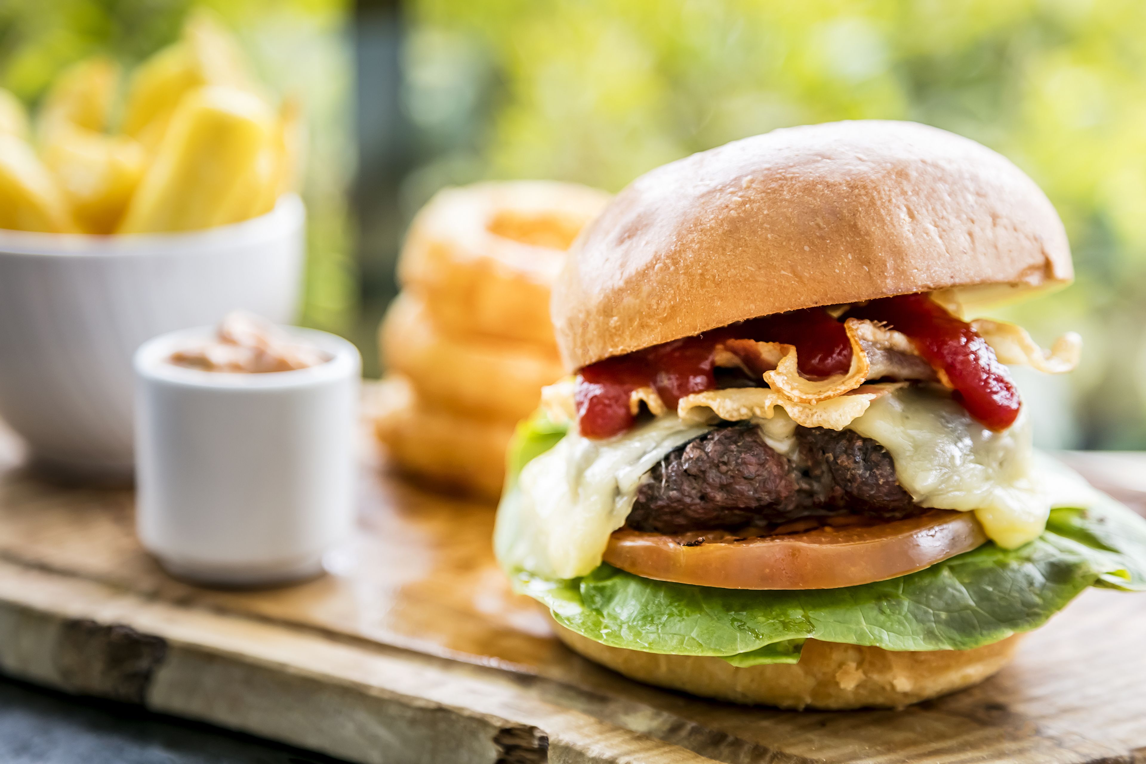 A burger with lettuce, cheese, and a bun, accompanied by fries and a small bowl of sauce.