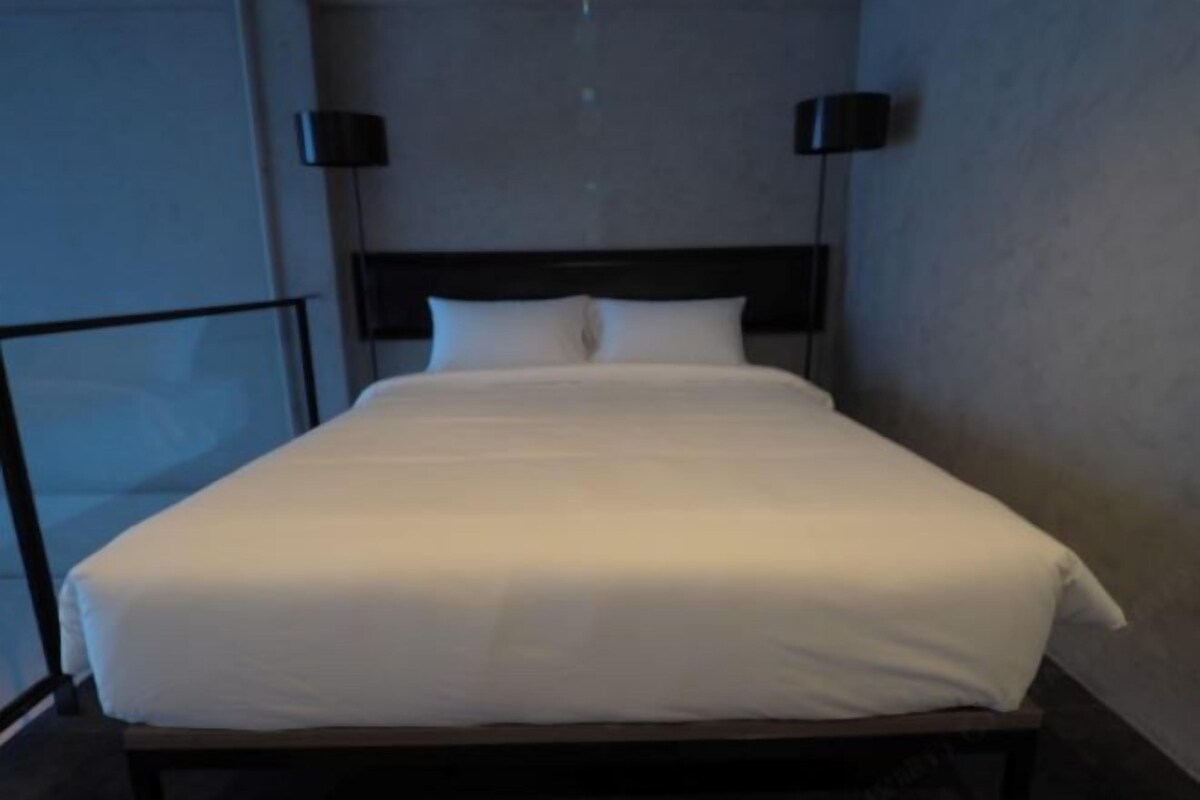 A neatly made bed with white linens in a room with a dark headboard and two wall-mounted lamps.