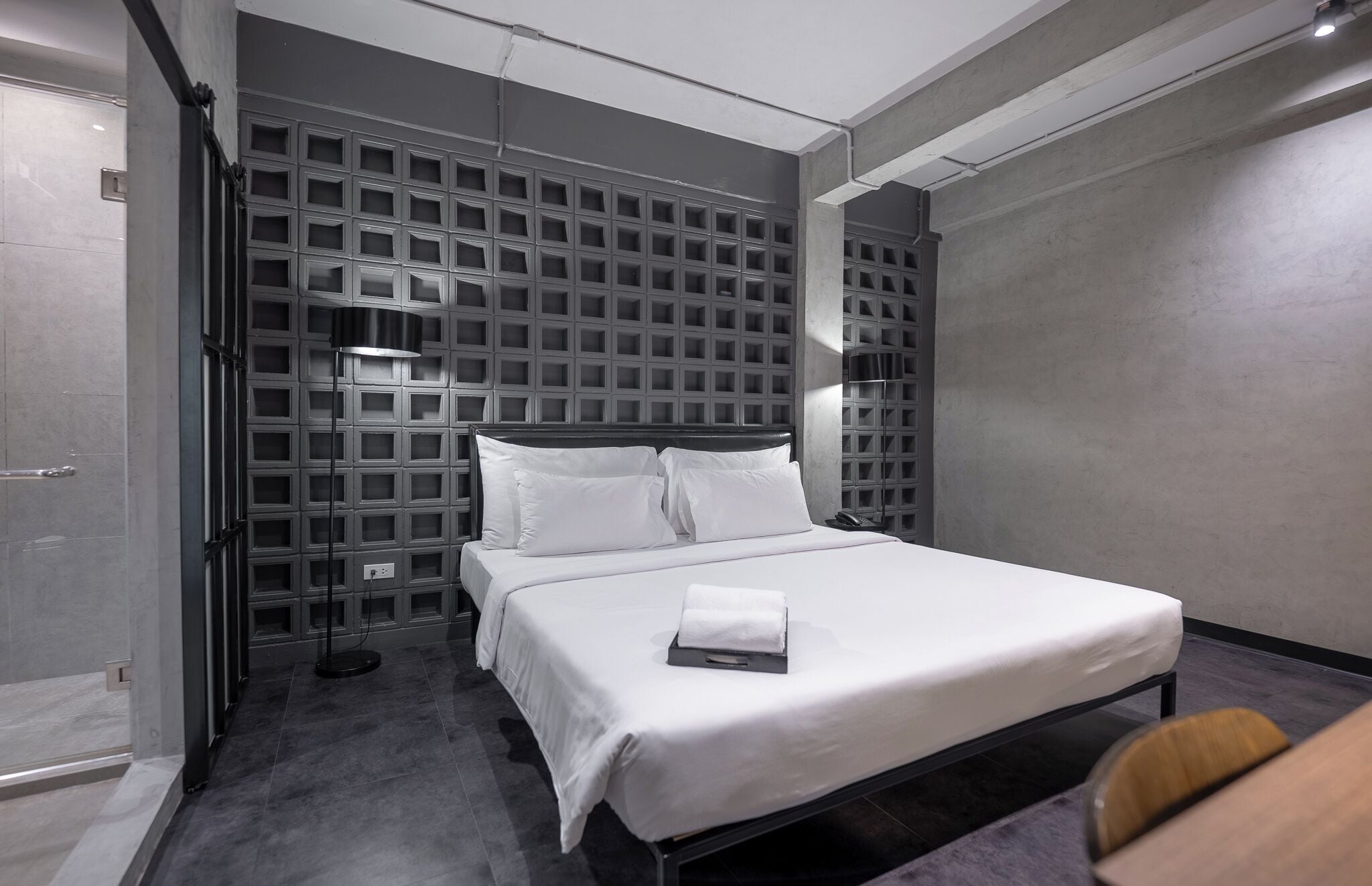A modern hotel room with a bed, a bedside table, a lamp, and a wall with a grid pattern.