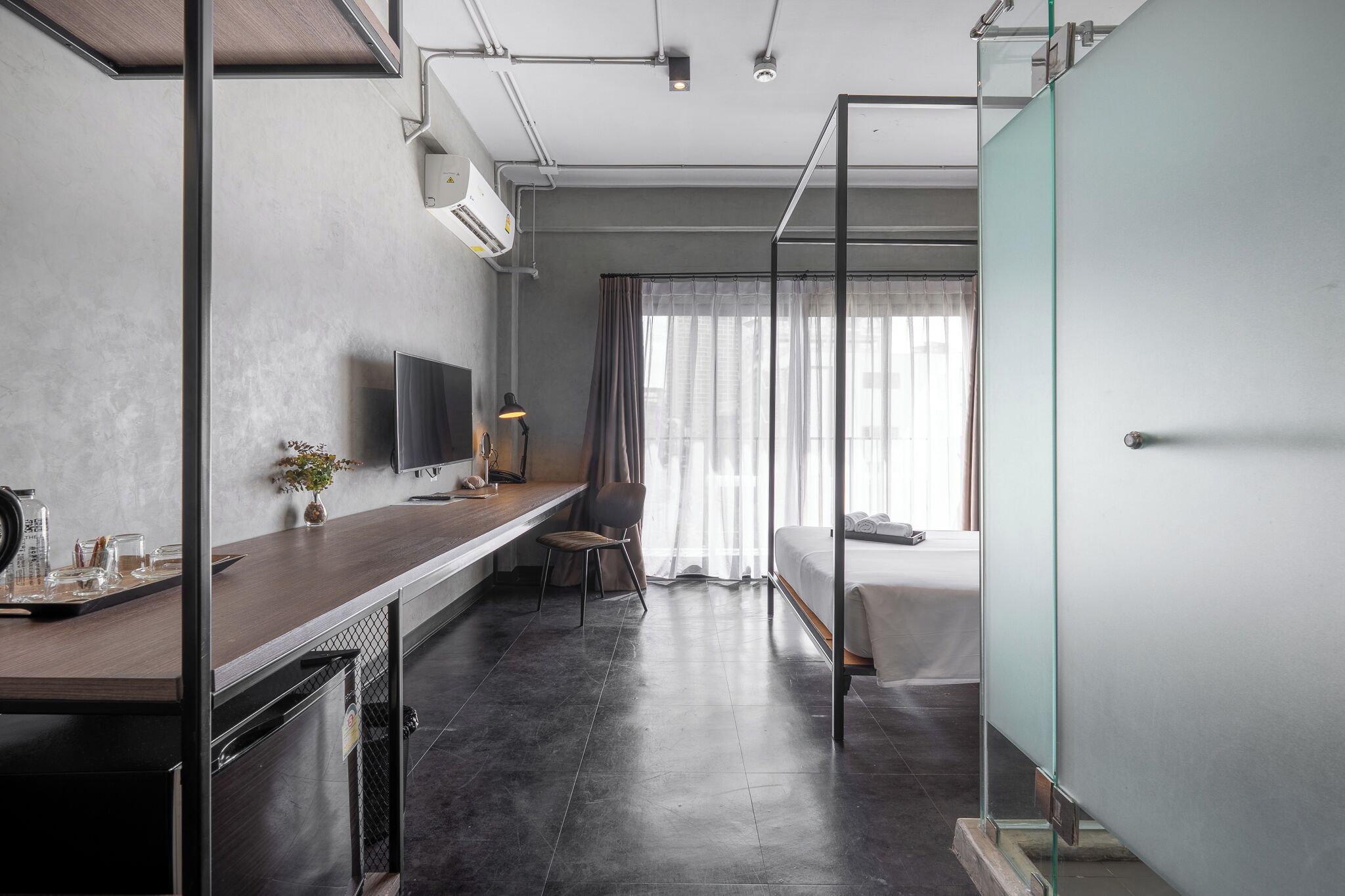 A modern hotel room with a kitchenette, a bed, a TV, and a large window with curtains.