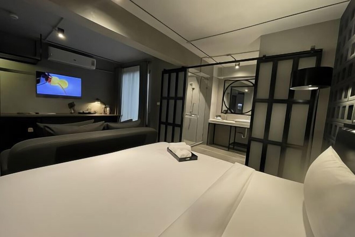 A modern hotel room with a large bed, a TV, a desk, and a bathroom.