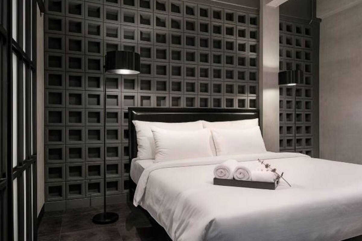 A modern hotel room with a large bed, a black headboard, and a wall with a grid pattern.
