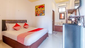A hotel room with a large bed, a painting on the wall, a bathroom with a sink and mirror, and a TV mounted on the wall. - OYO 401 The Frog Homestay Sanur (Denpasar)