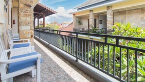 A balcony with white chairs, a stone pillar, and a view of a building with a tiled roof. - OYO 401 The Frog Homestay Sanur (Denpasar)